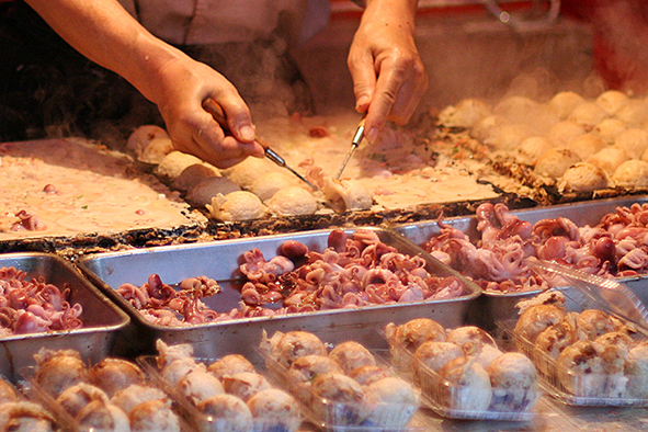 Takoyaki being prepared at a street - side establishment (Photo: D'n'c via Flickr)