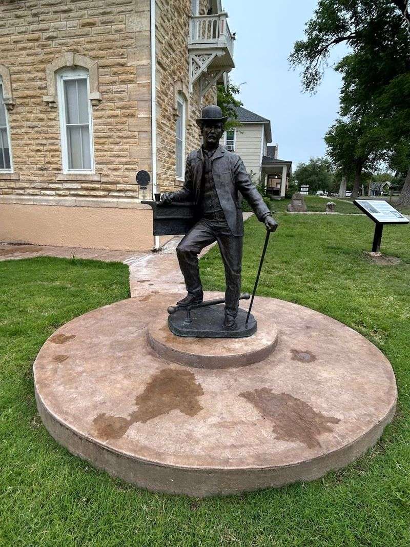 A Bronze Statue Of Bat Masterson Stands On The Lawn